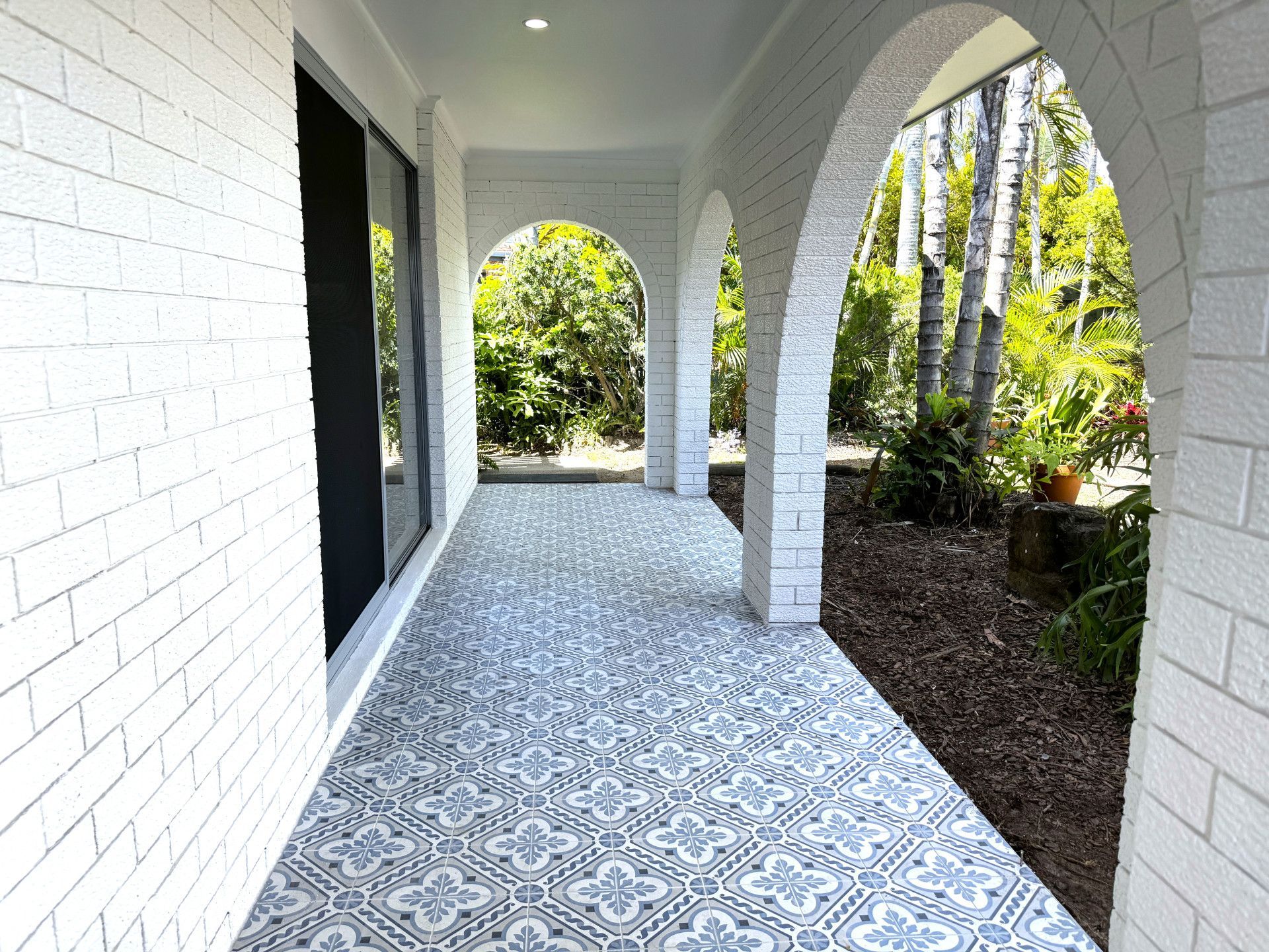 Covered porch with white brick and patterned tile flooring, arched entryways, and lush greenery. — Nyblad Construction in Maroochydore, QLD
