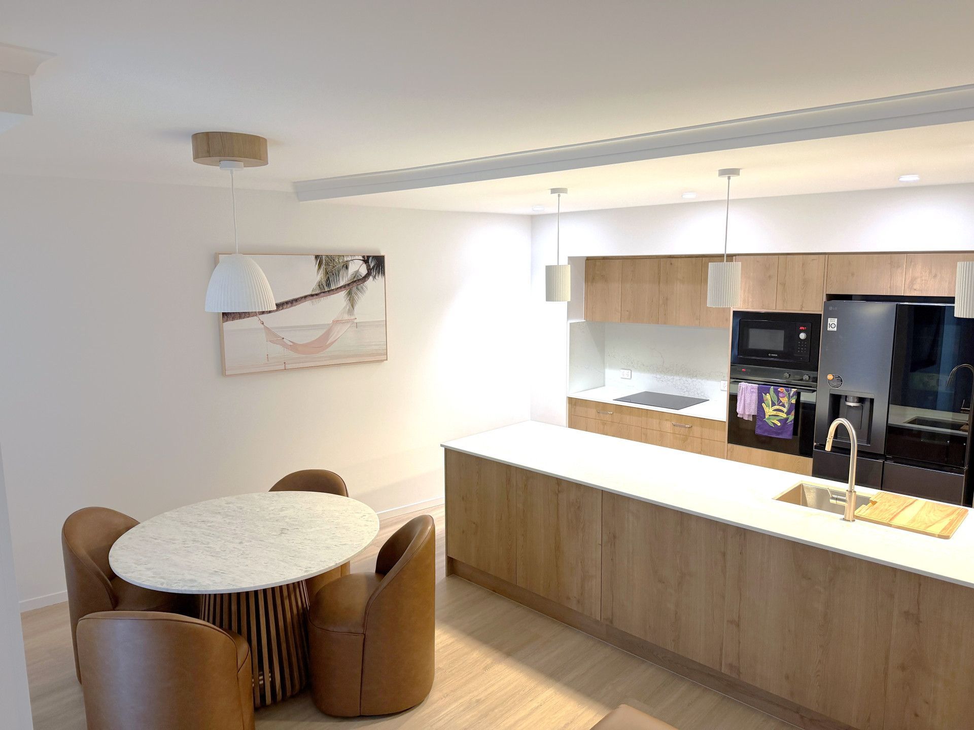 Modern kitchen with light wood cabinets, white countertops, and a dining table with four brown chairs. — Nyblad Construction in Coolum, QLD