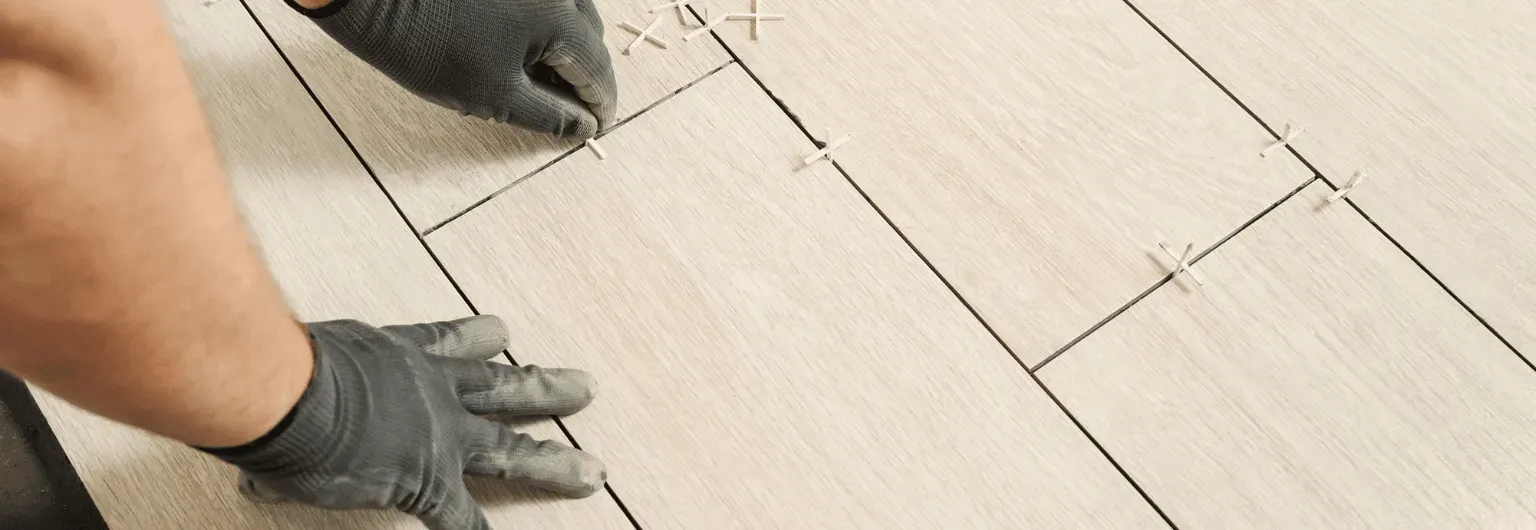 A Person Is Laying Tiles On A Wooden Floor — Nyblad Construction in Caloundra West, QLD