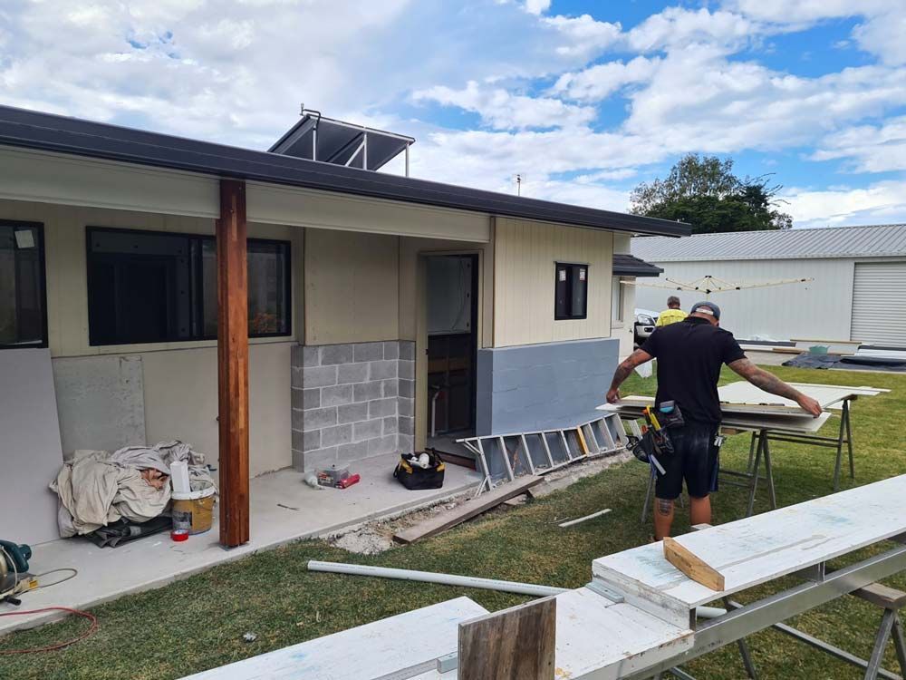 A Man Is Standing In Front Of A House Holding A Ladder — Nyblad Construction in Caloundra West, QLD