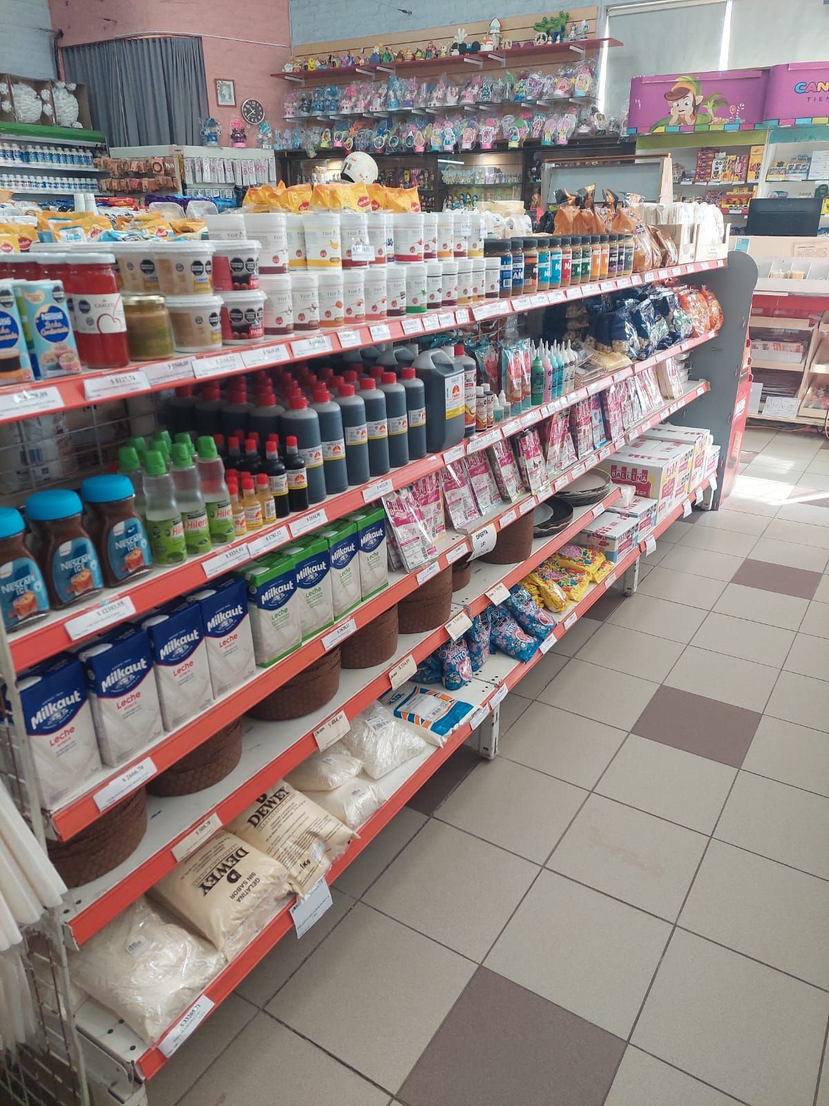 Un pasillo de supermercado con estantes llenos de aperitivos, bebidas y productos envasados ​​sobre un suelo de baldosas.