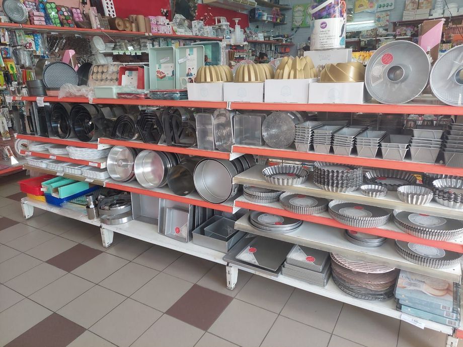 Estanterías repletas de utensilios de cocina y vajilla en un pasillo de una tienda, con platos, cuencos y ollas apilados.