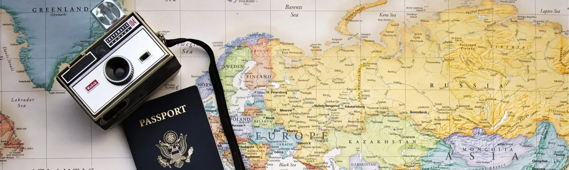 Passport, camera, and suitcase on a world map, suggesting travel planning