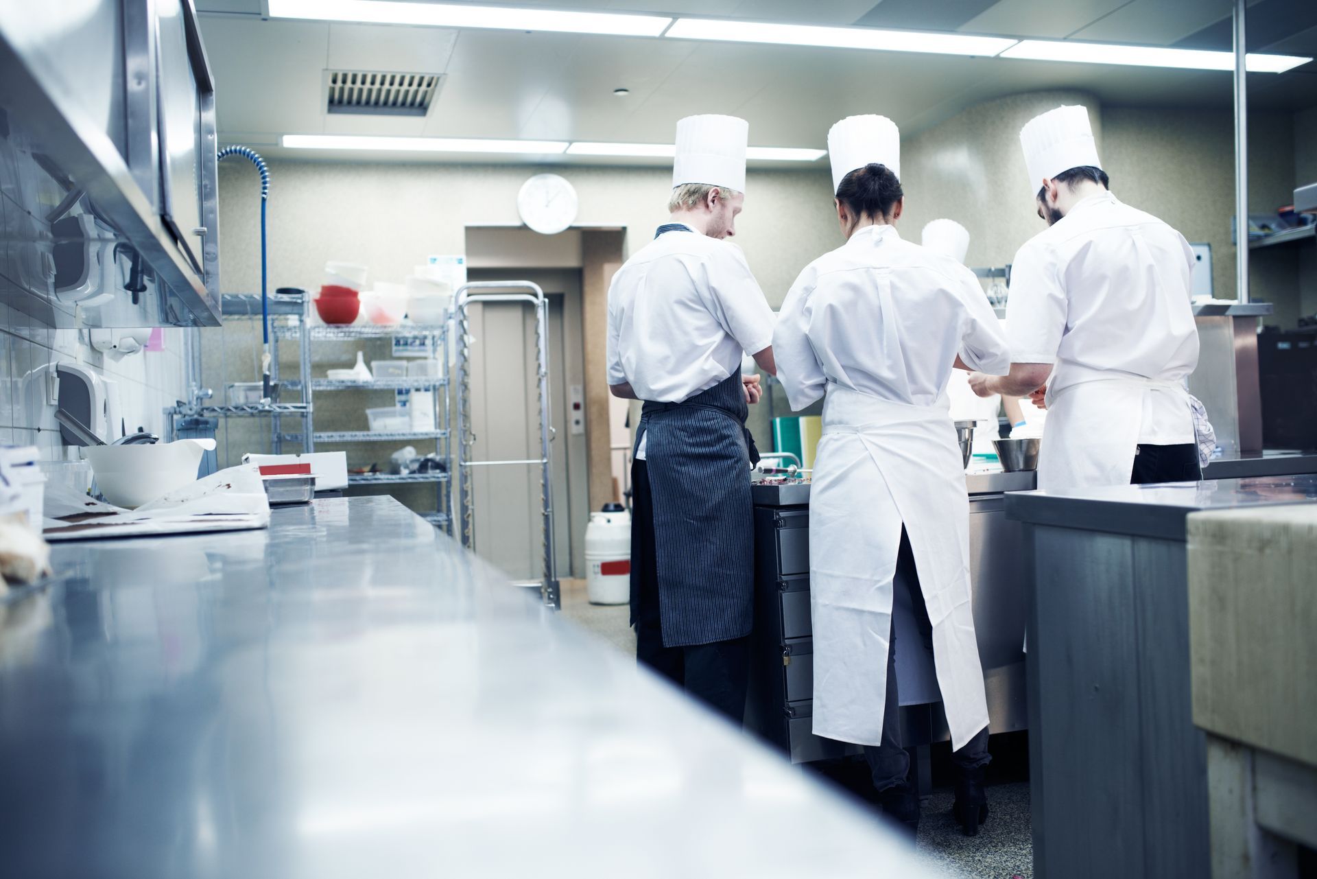 Chefs in white uniforms working in a stainless-steel commercial kitchen