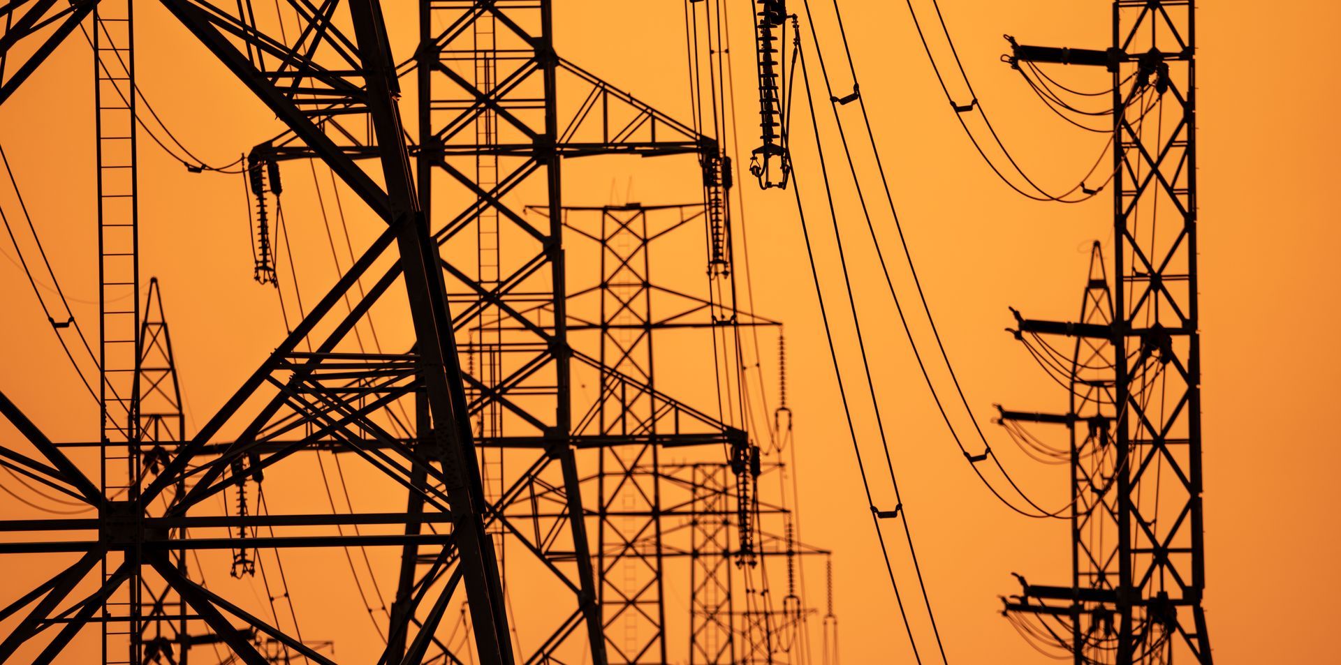 Silhouetted power lines and utility towers against an orange sky