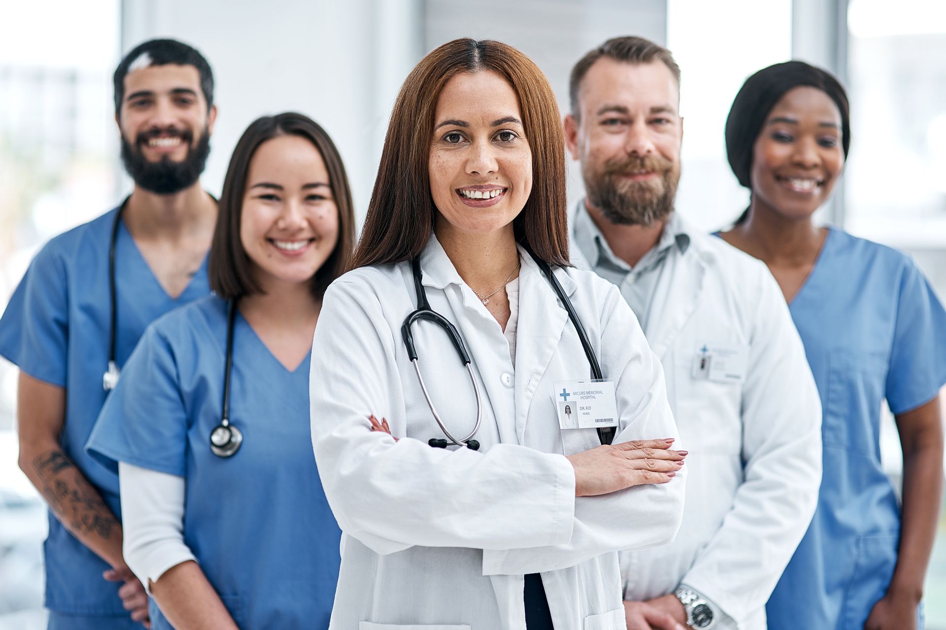 Medical team in scrubs and lab coats standing together, led by a doctor with arms crossed and a stethoscope.