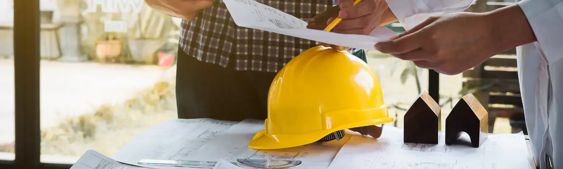 Construction worker reviewing blueprints beside a yellow hard hat on a table
