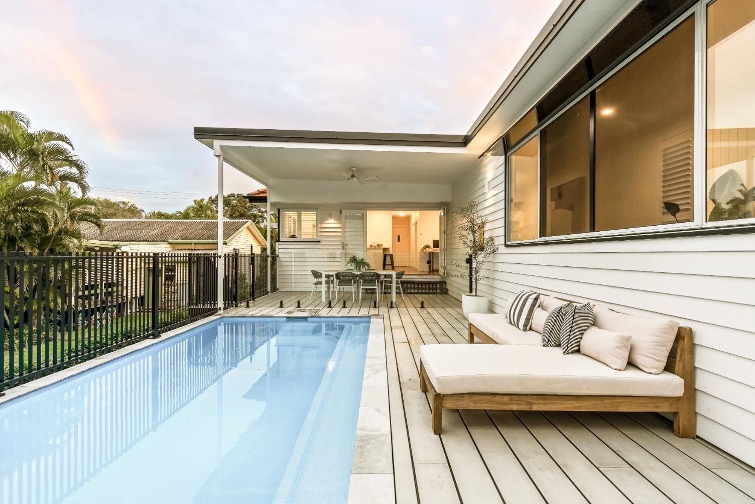 Modern patio with a swimming pool, white lounge chair, and covered outdoor seating beside a house