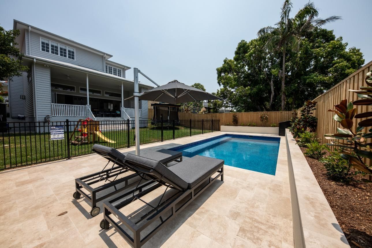 Backyard pool with two lounge chairs, patio, and modern house on a sunny day