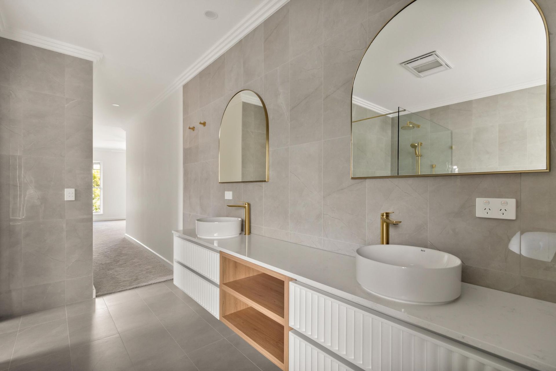 Modern bathroom with double vanity, arched mirrors, light gray tile, and a walk-in shower.