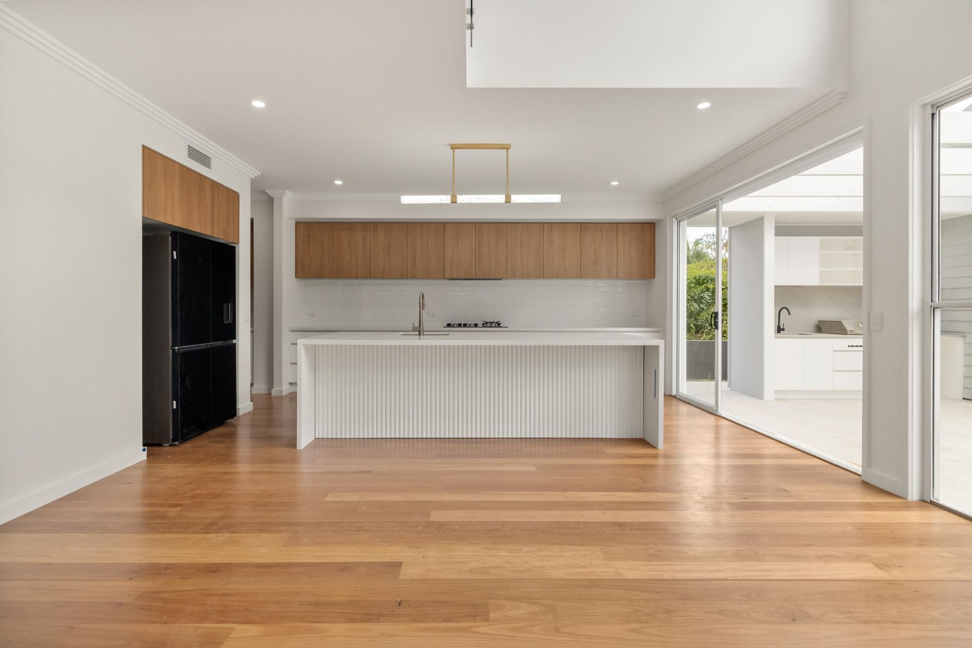 Bright modern kitchen with wood floors, white island, black refrigerator, and floor-to-ceiling windows
