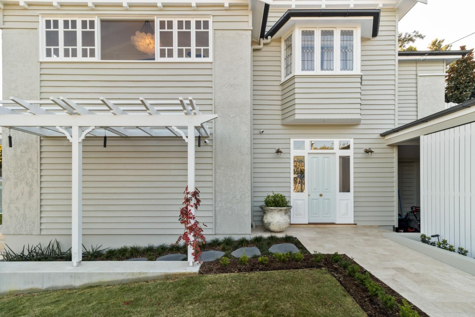 Exterior of a beige townhouse with white trim, front door, garage, and small lawn with trellis