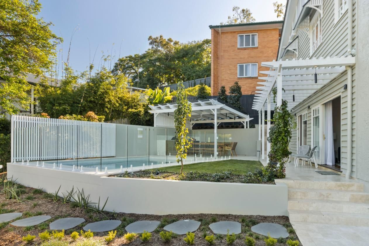 Modern house patio with pool, white pergola, and curved white wall amid greenery