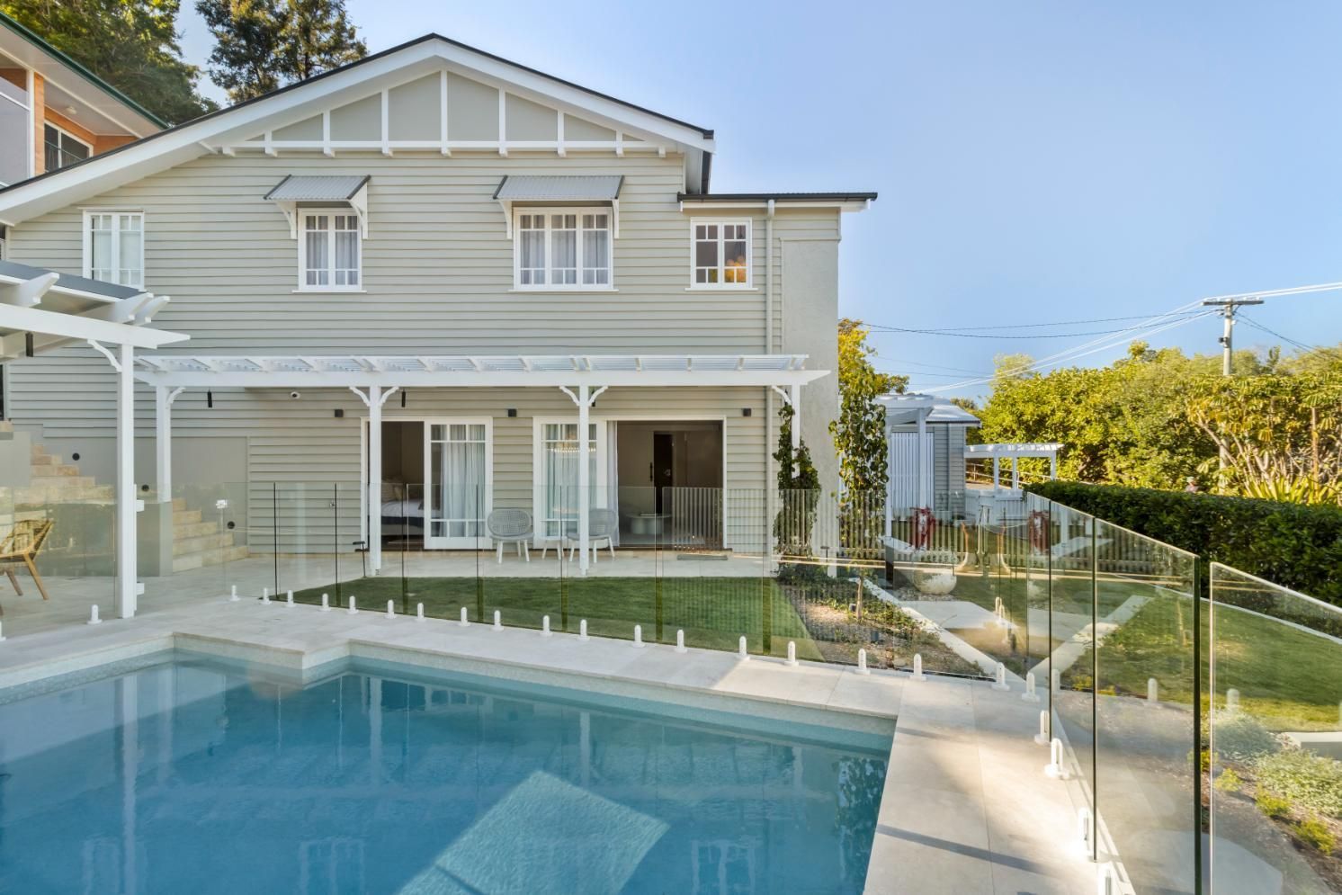 Backyard pool beside a gray house with a covered patio and glass railing at sunset
