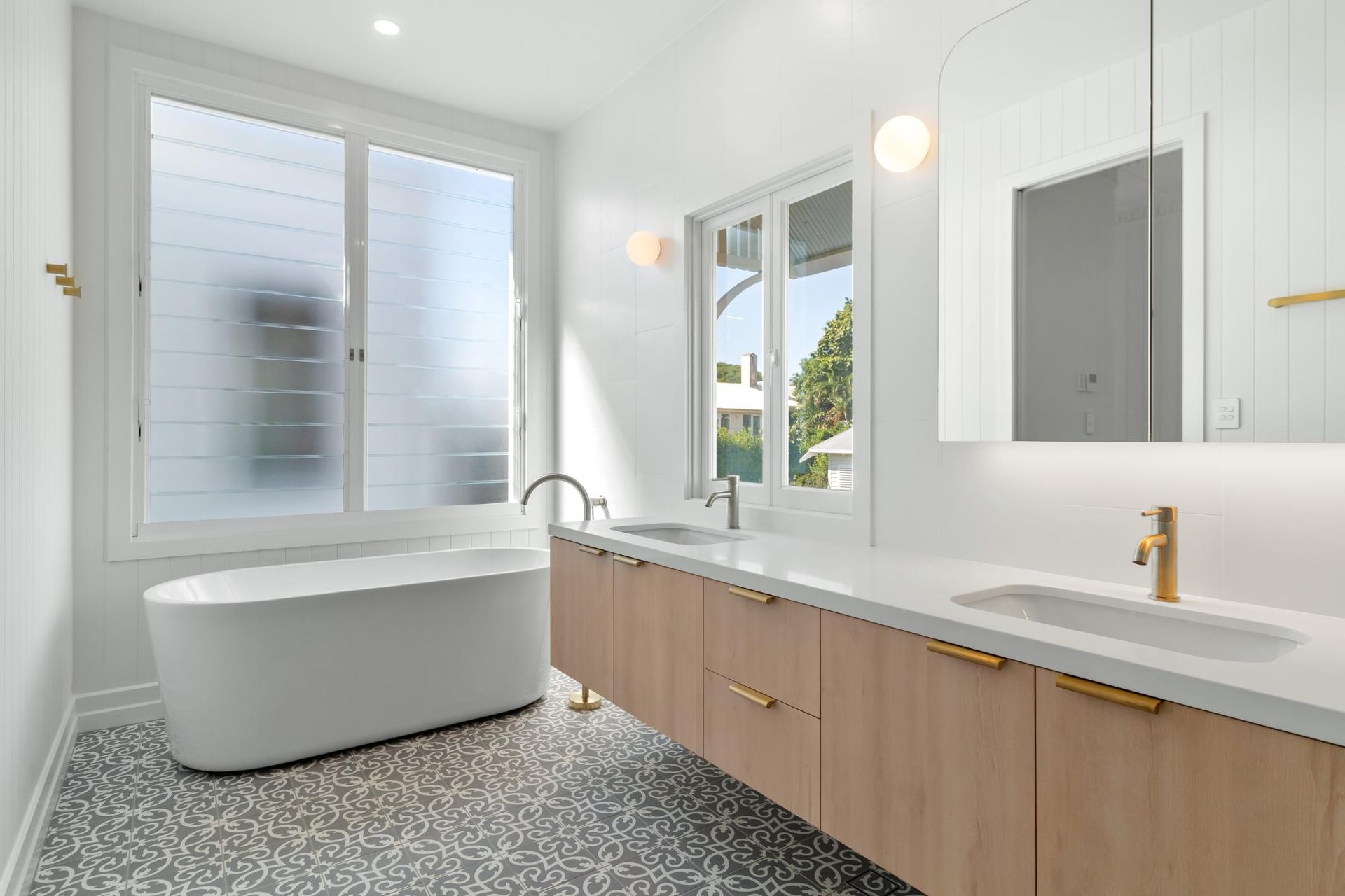 Bright modern bathroom with freestanding tub, double vanity, large window, and speckled black-and-white floor
