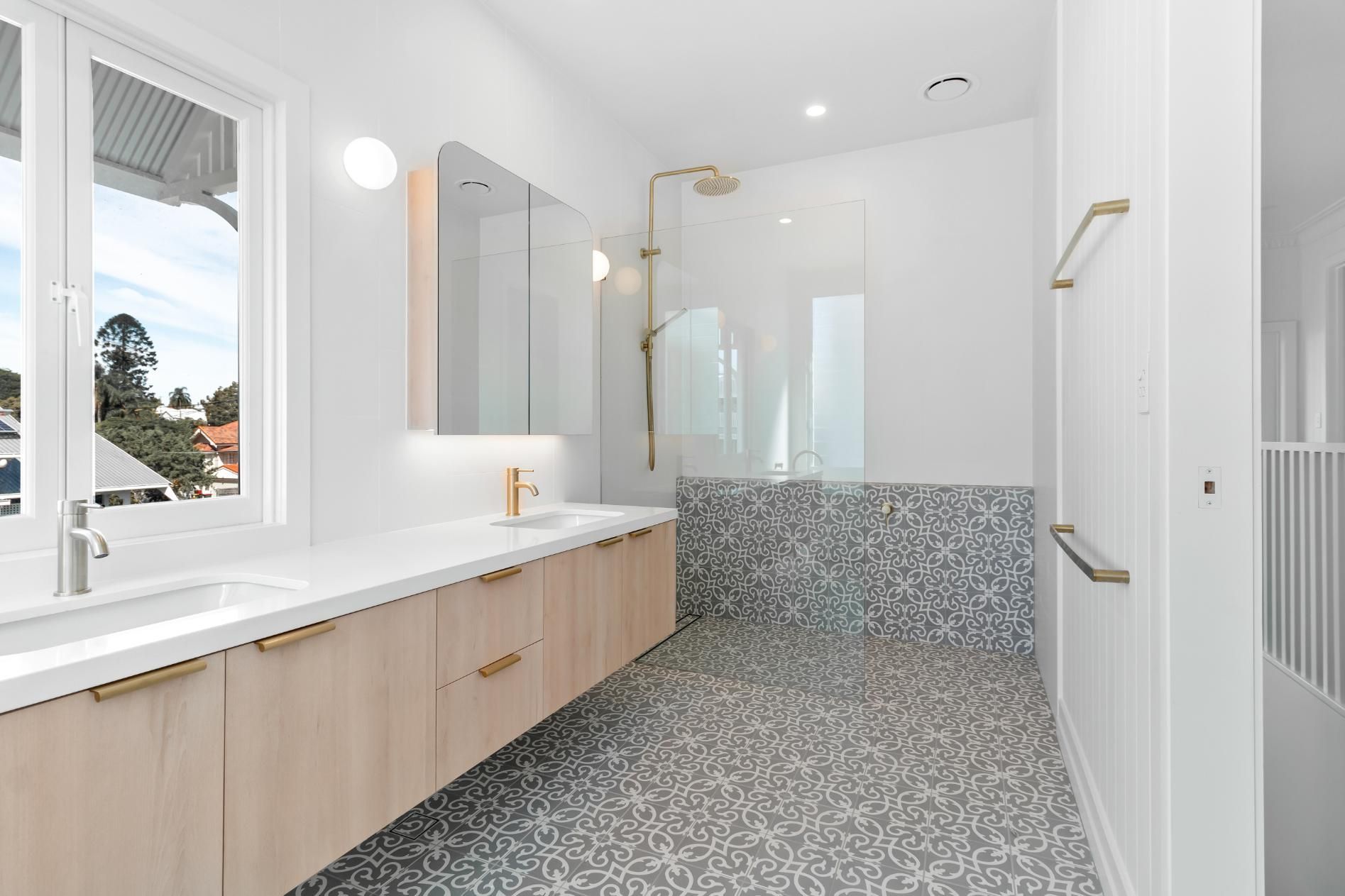 Bright modern bathroom with double vanity, large window, and glass-enclosed shower.