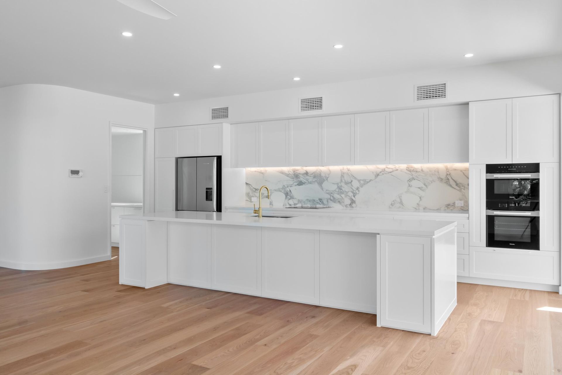 Modern white kitchen with marble backsplash, stainless appliances, and light wood flooring