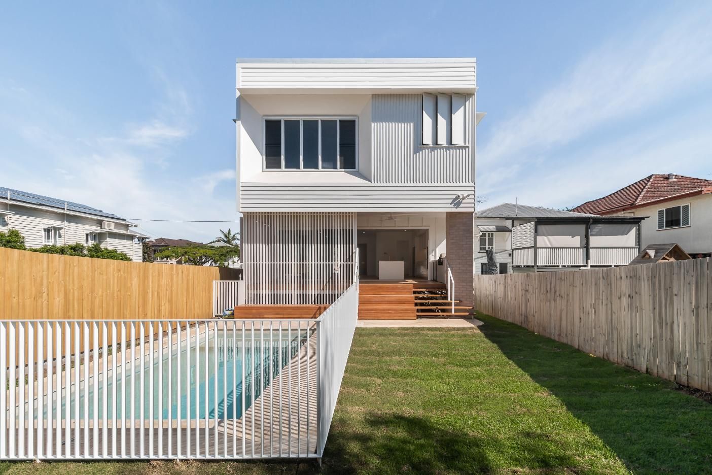 Modern two-story white house with a backyard pool, lawn, and wooden fence