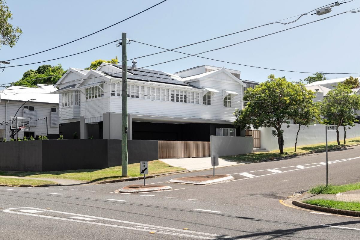 White two-story house on a corner with a black fence, trees, and overhead power lines on a sunny day