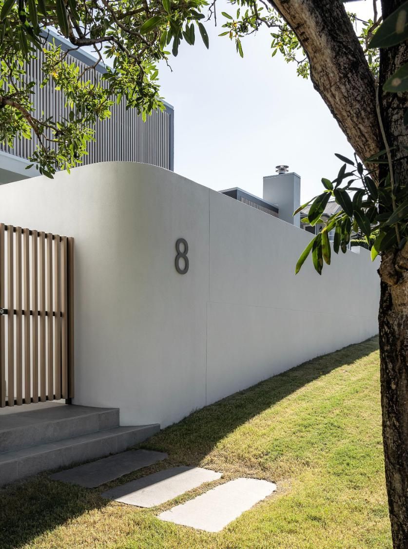 White house wall with number 8, wooden gate, and steps under tree shade in a sunny yard.