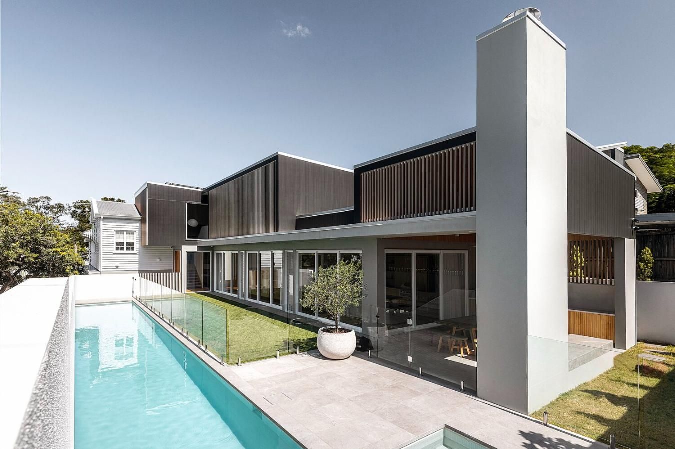 Modern house with a long turquoise pool, glass walls, and a white tower under a clear sky