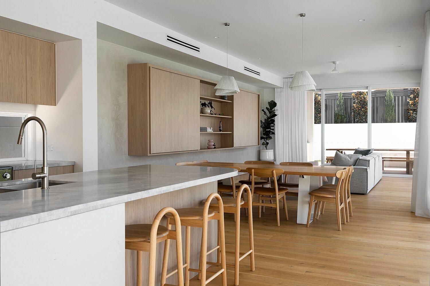 Modern open-plan kitchen and dining area with light wood floors, marble island, and large windows