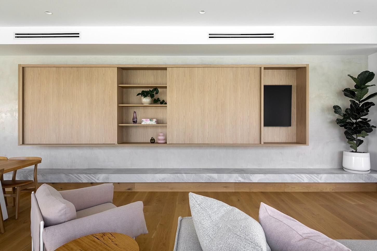 Modern living room with light wood wall cabinets, a built-in shelf, and neutral sofas on a wood floor.