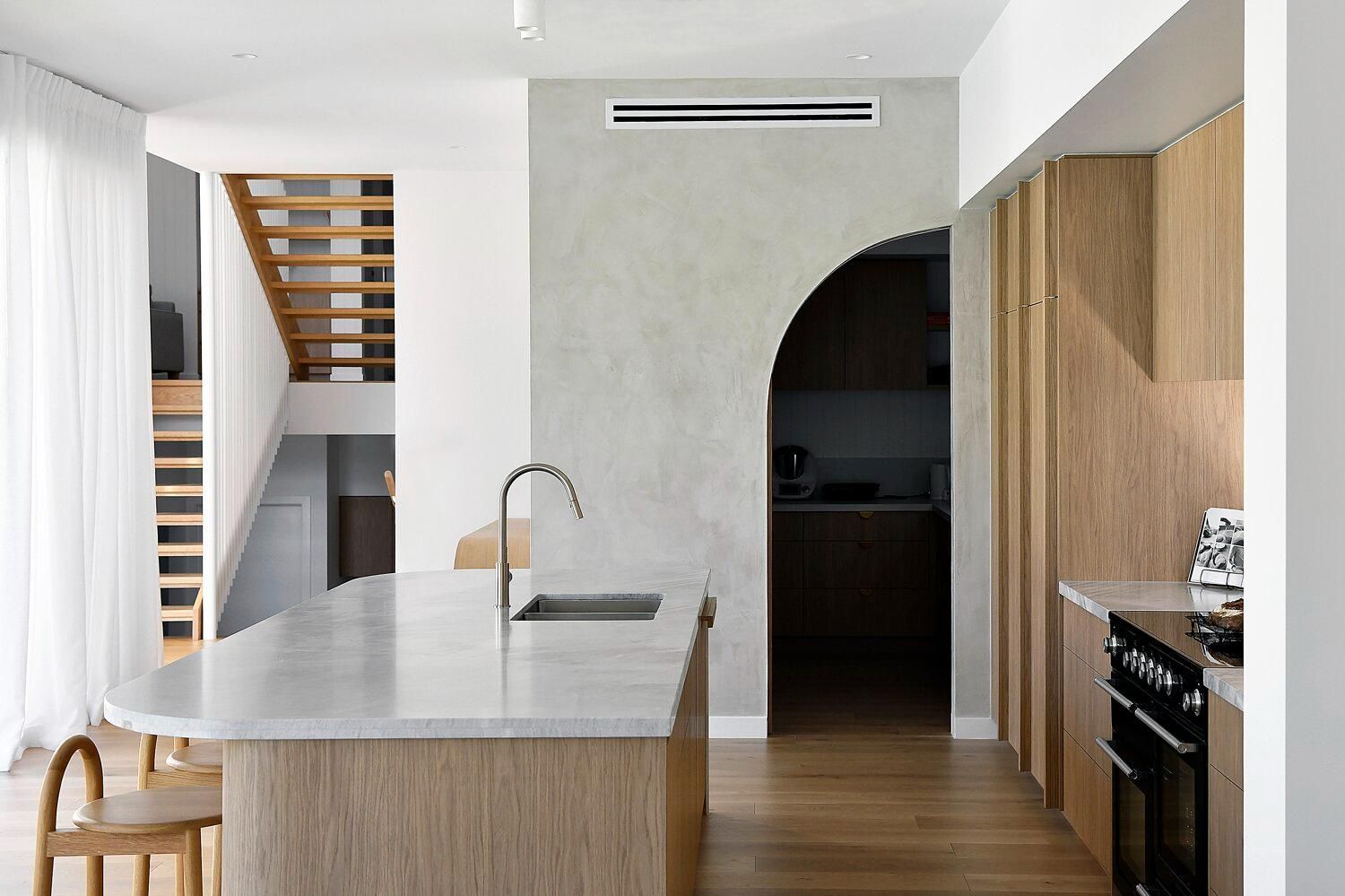 Modern kitchen with a marble island, wood cabinets, and a dark arched doorway leading to another room