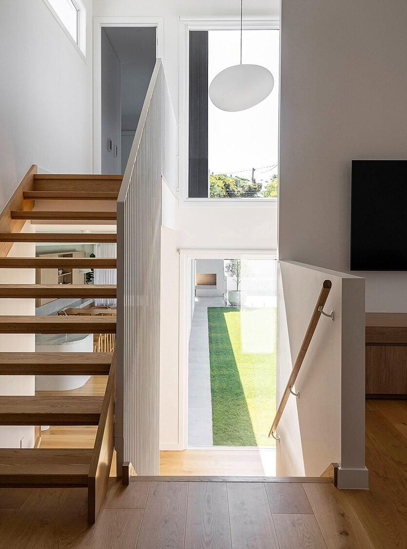 Modern stairway landing with wooden steps, white railing, and a view to a bright backyard through a large window.