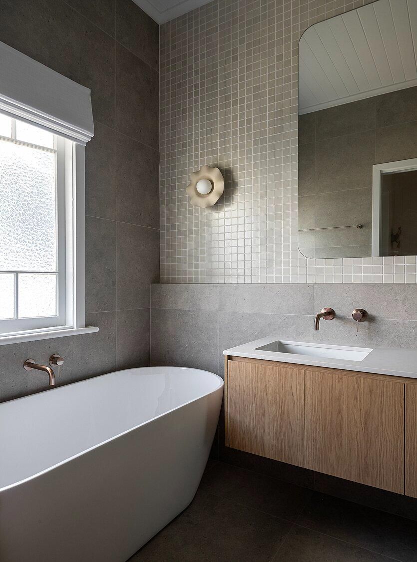 Small modern bathroom with freestanding tub, wood vanity, and textured tile walls