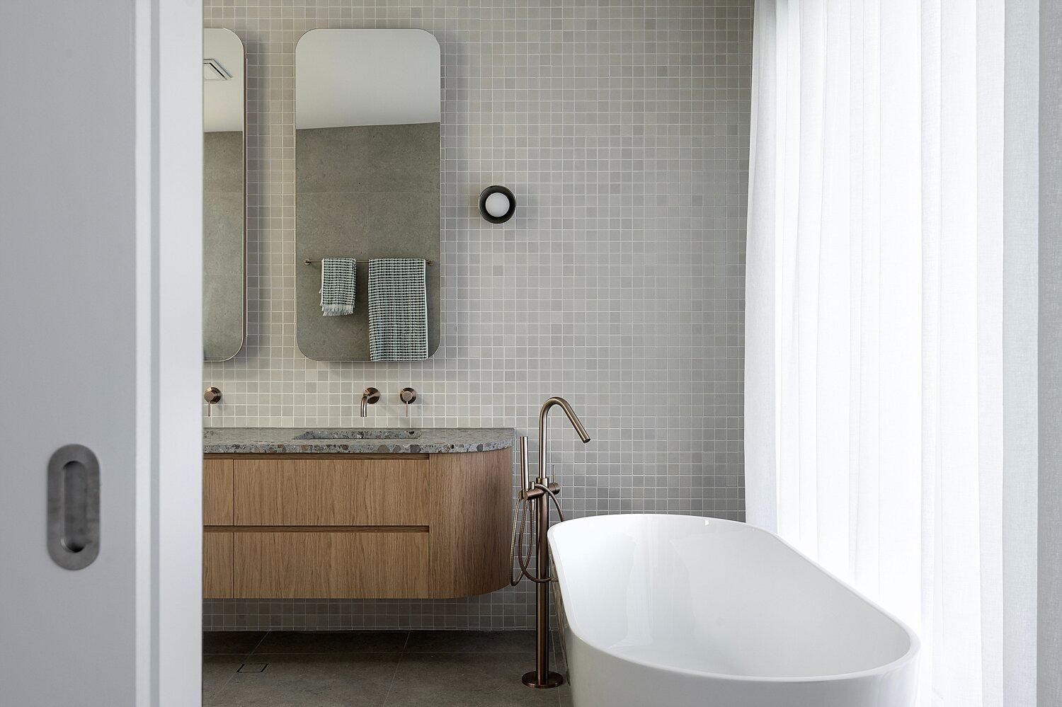Modern bathroom with wood vanity, round mirror, tiled wall, and white bathtub by a shower curtain