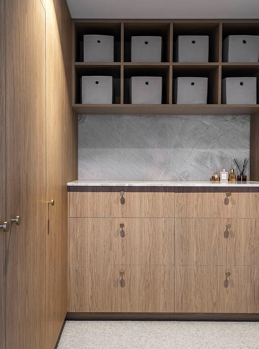 Built-in wooden storage nook with shelves, gray bins, and a countertop under a stone backsplash.