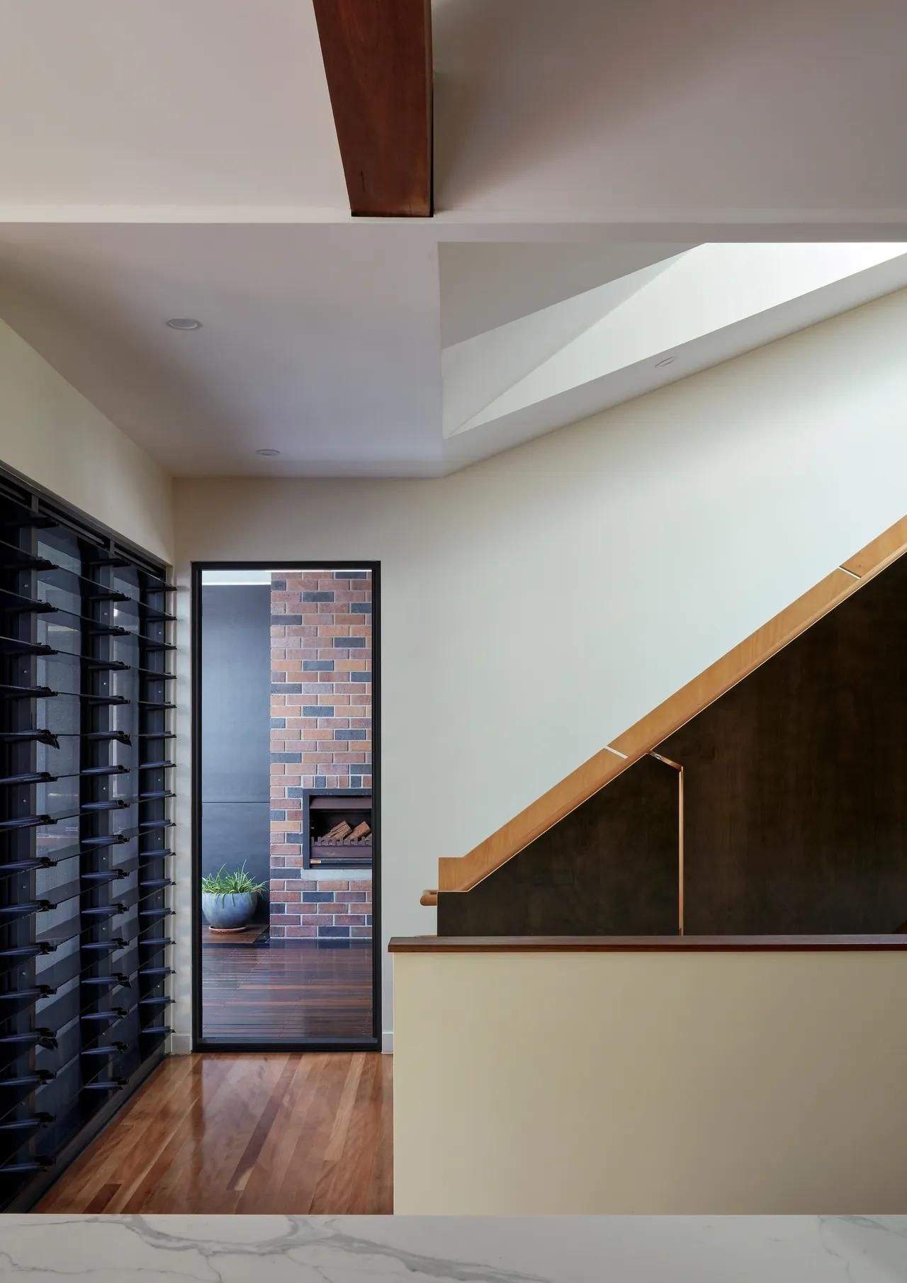 Modern interior hallway with wood floor, black shelving, and staircase with a skylight.