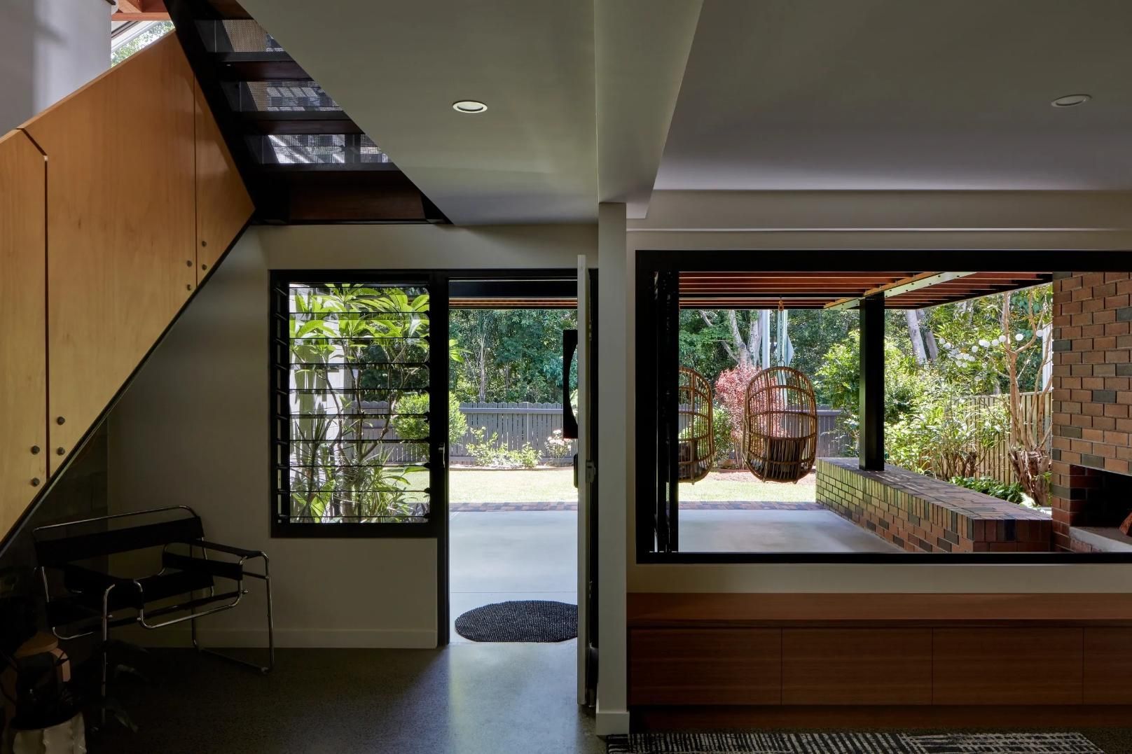 Modern home interior with staircase, piano, and open sliding doors to a leafy patio and garden.