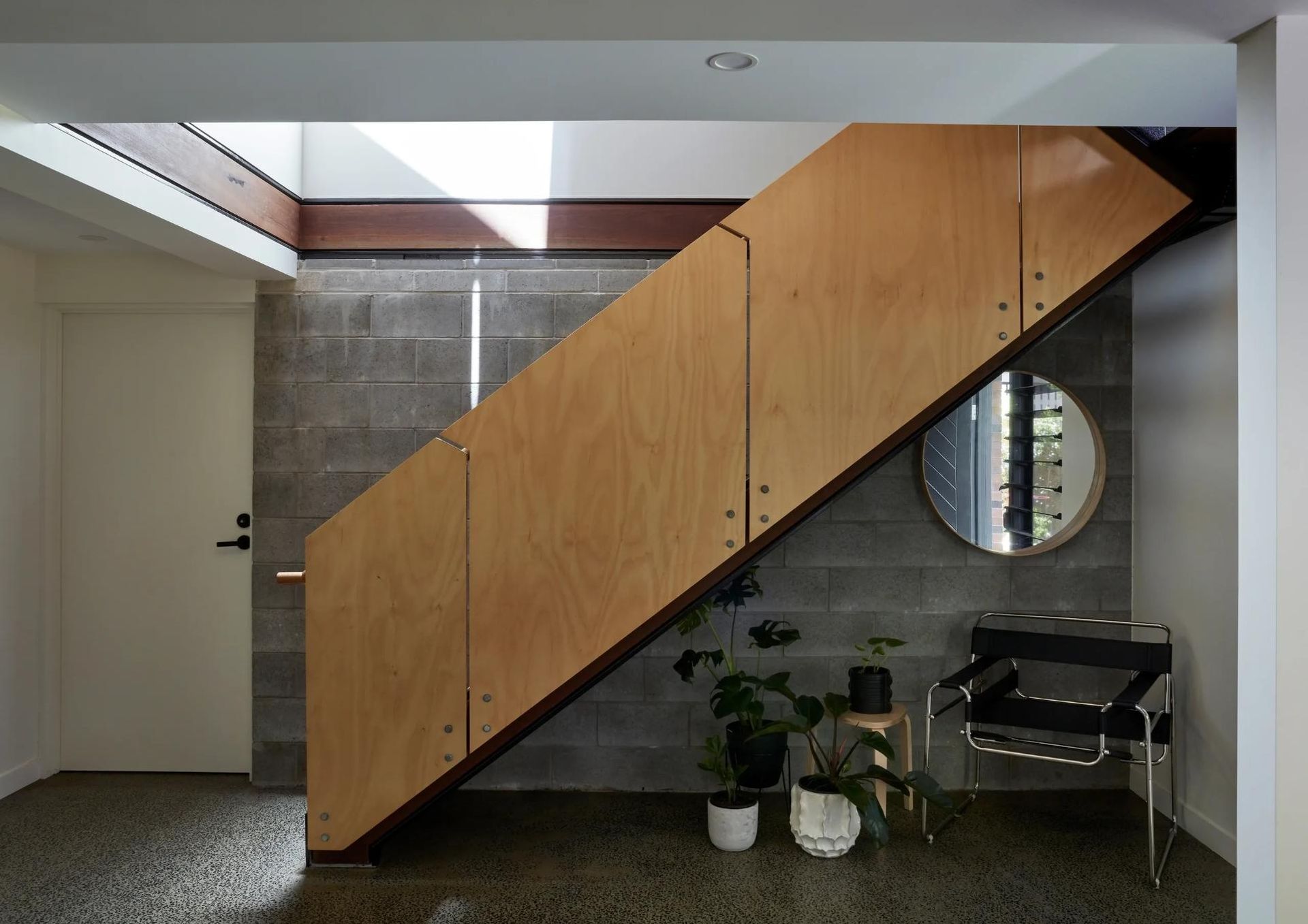Under-stair wooden storage cabinets in a modern interior with a round mirror and plants