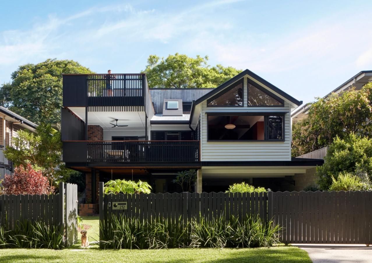 Two-story modern house with black and white exterior, front fence, and green trees under a bright sky