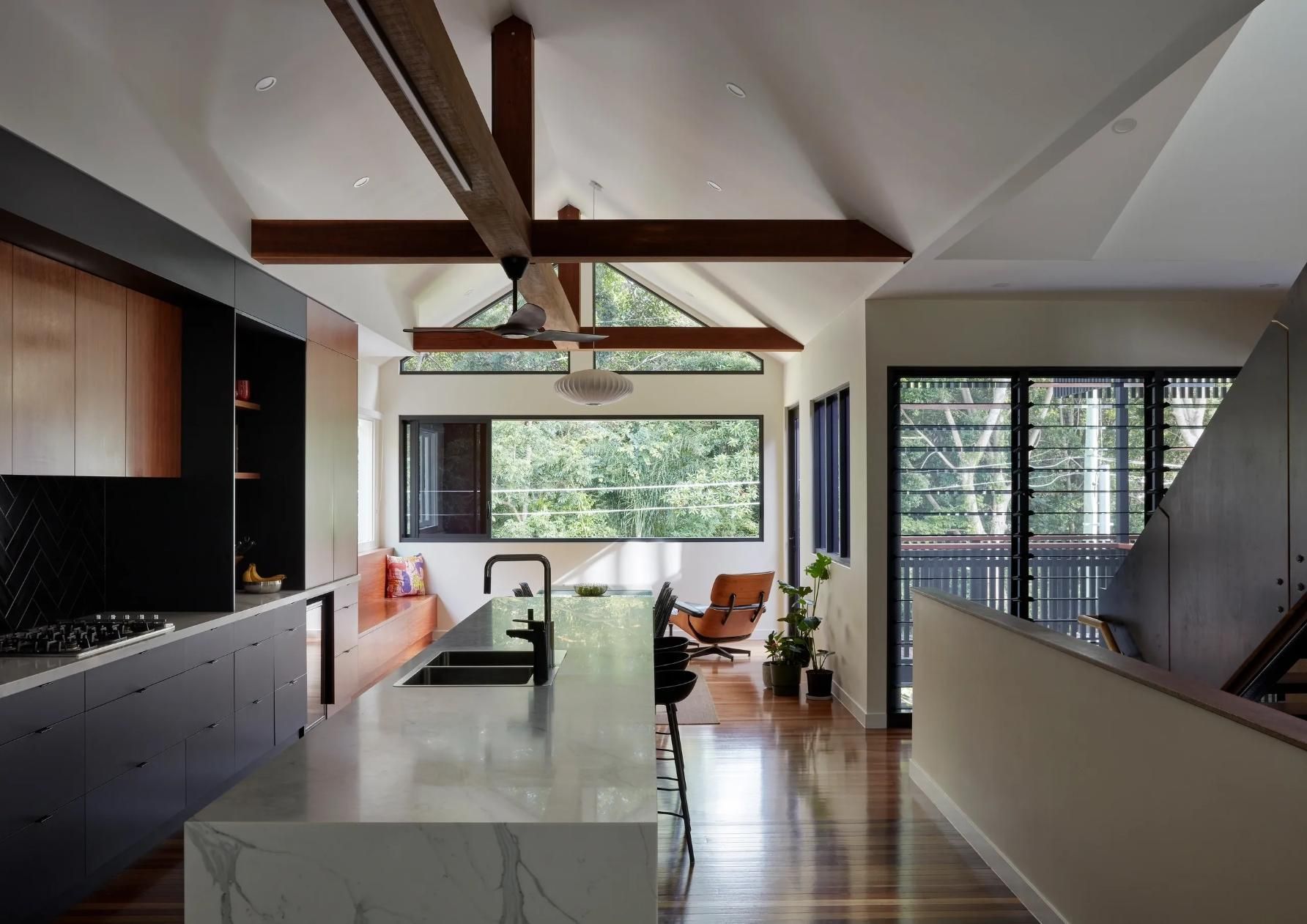 Modern open-plan kitchen and living area with marble island, wood beams, ceiling fan, and large windows