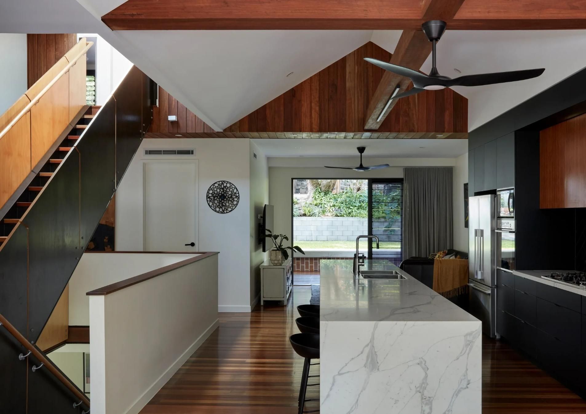 Modern kitchen and living space with wood beams, marble island, staircase, and large glass doors