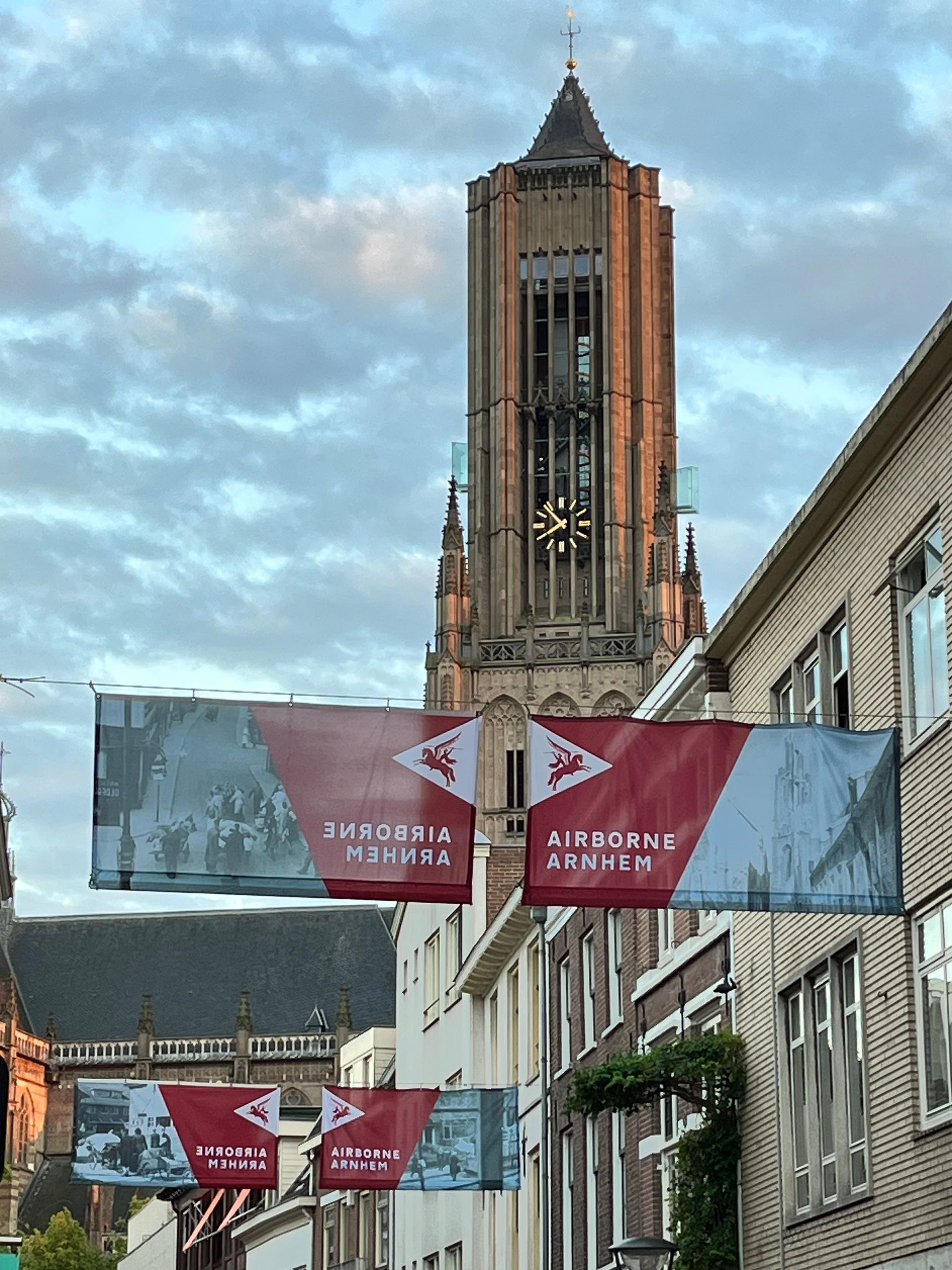 Eusebiuskerk Arnhem met Airborne banners. Straatbanners op de campus onder een hoge bakstenen toren tegen een bewolkte hemel.