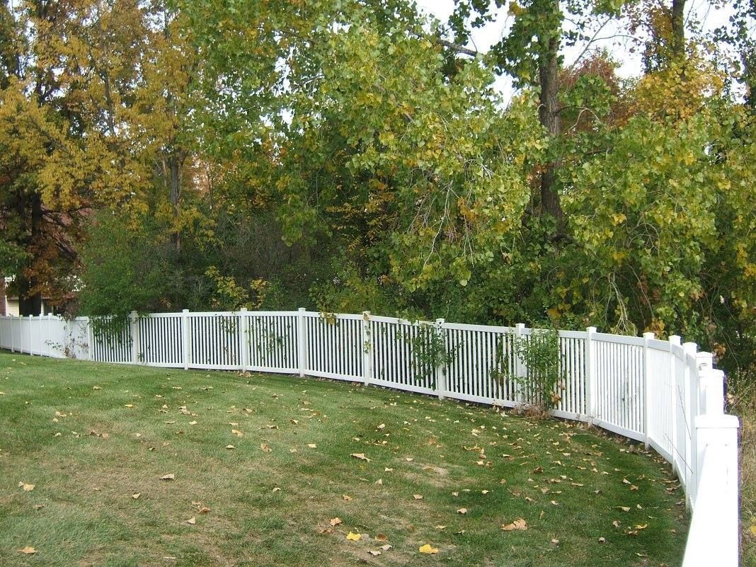 A white vinyl fence runs across a landscaped backyard with lawn and blue sky in the background. A white vinyl fence runs across a landscaped backyard with lawn and blue sky in the background.