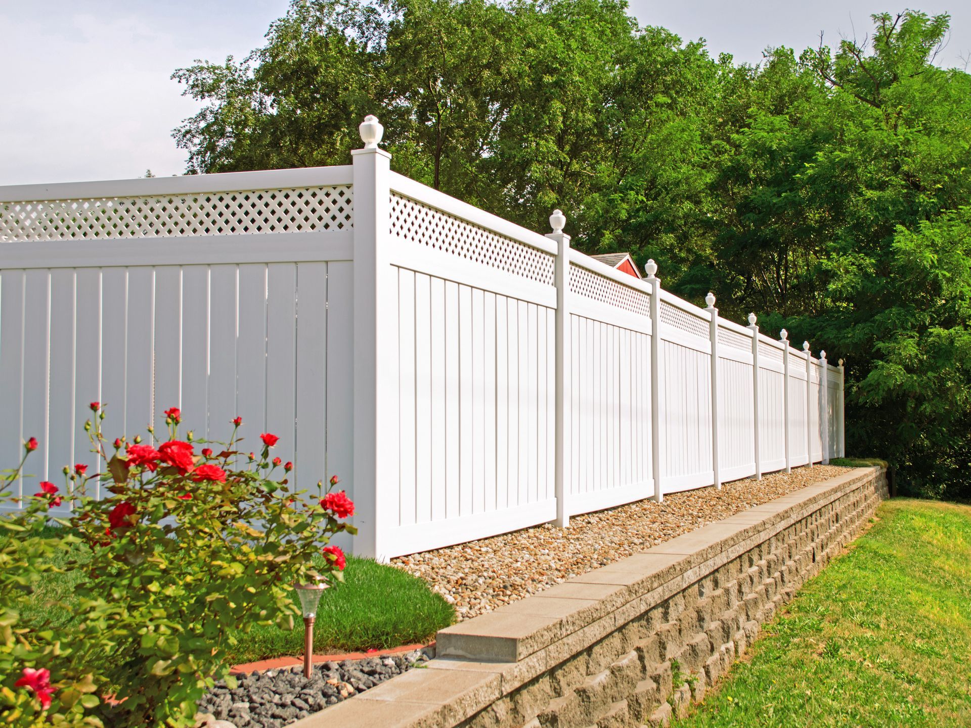 A white vinyl fence in a backyard with nice landscaping in the foreground and background.