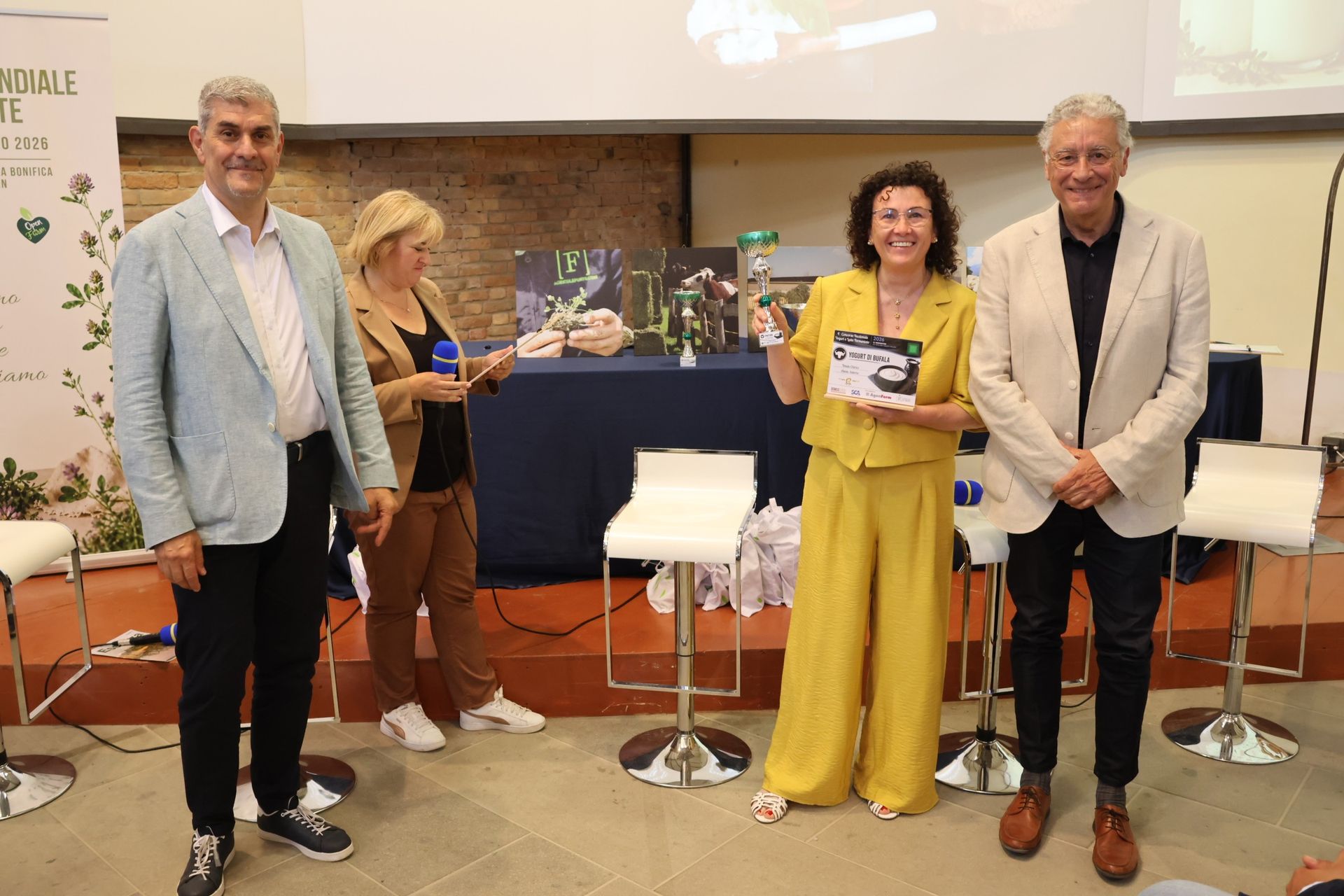 Quattro persone in piedi su un palco, due delle quali tengono in mano dei libri, durante una conferenza o una presentazione.