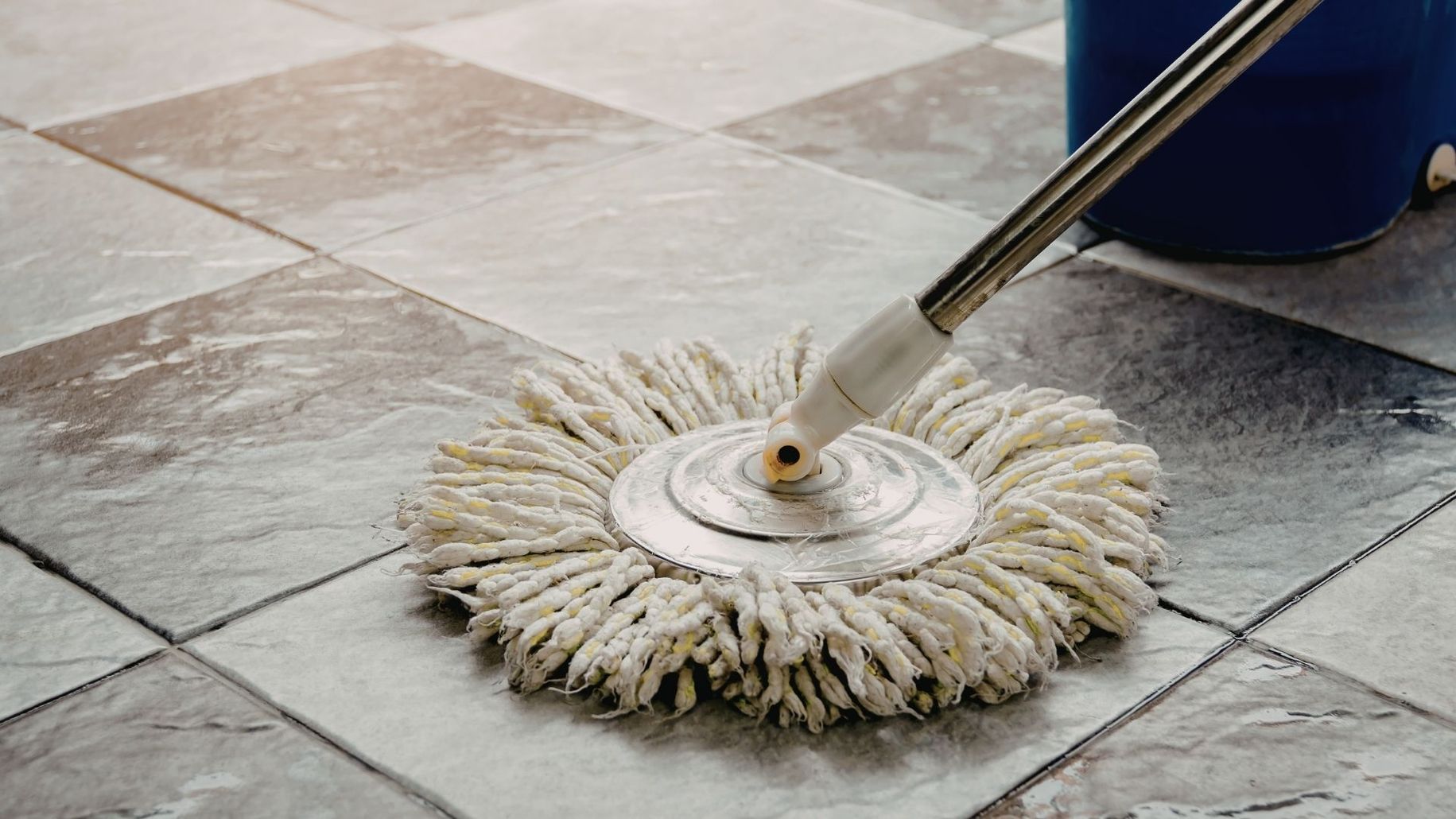 Mop head cleaning a tiled floor with visible wet grout lines and a mop handle attached