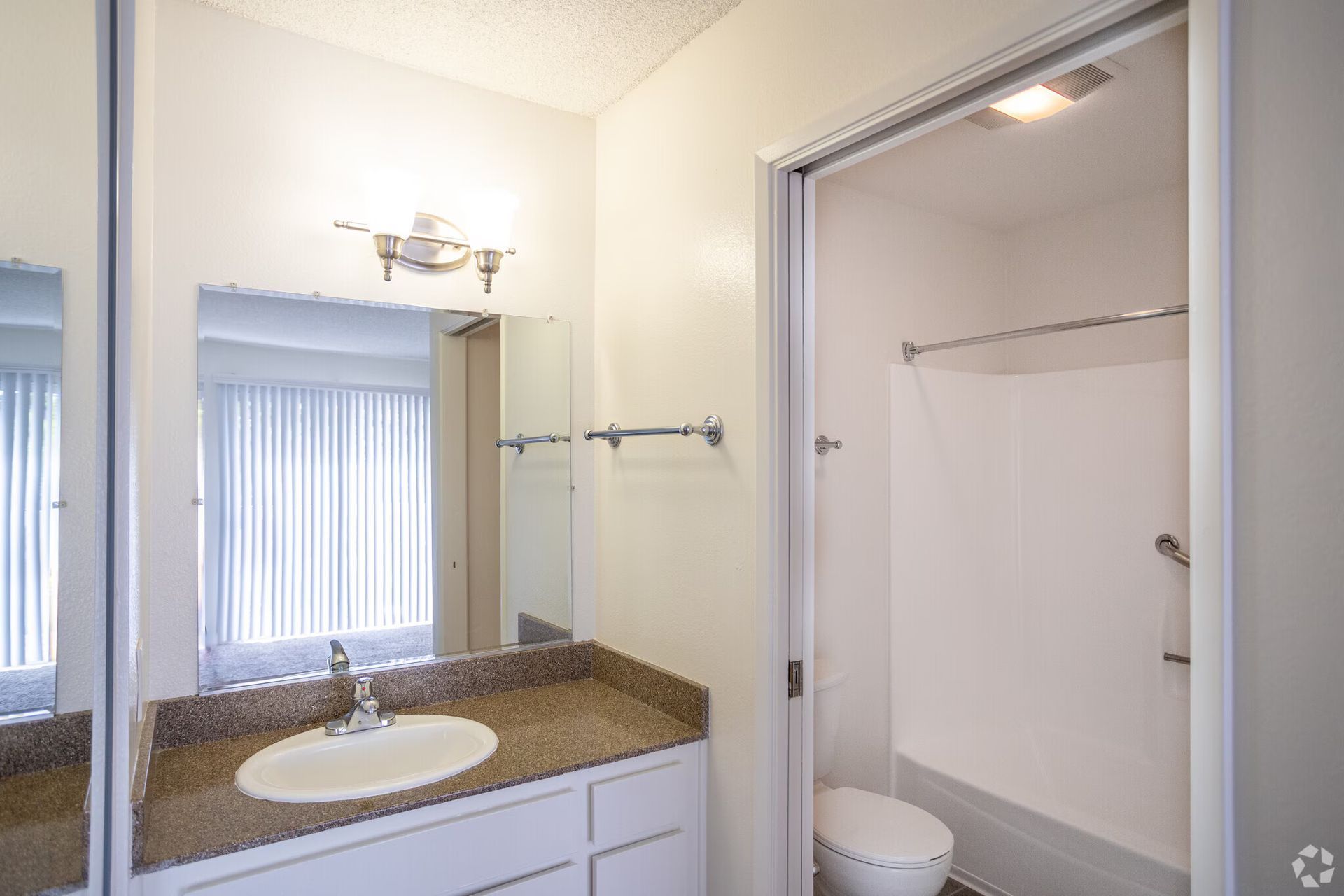 Bathroom vanity with mirror and sink beside an open closet or shower alcove with white walls.