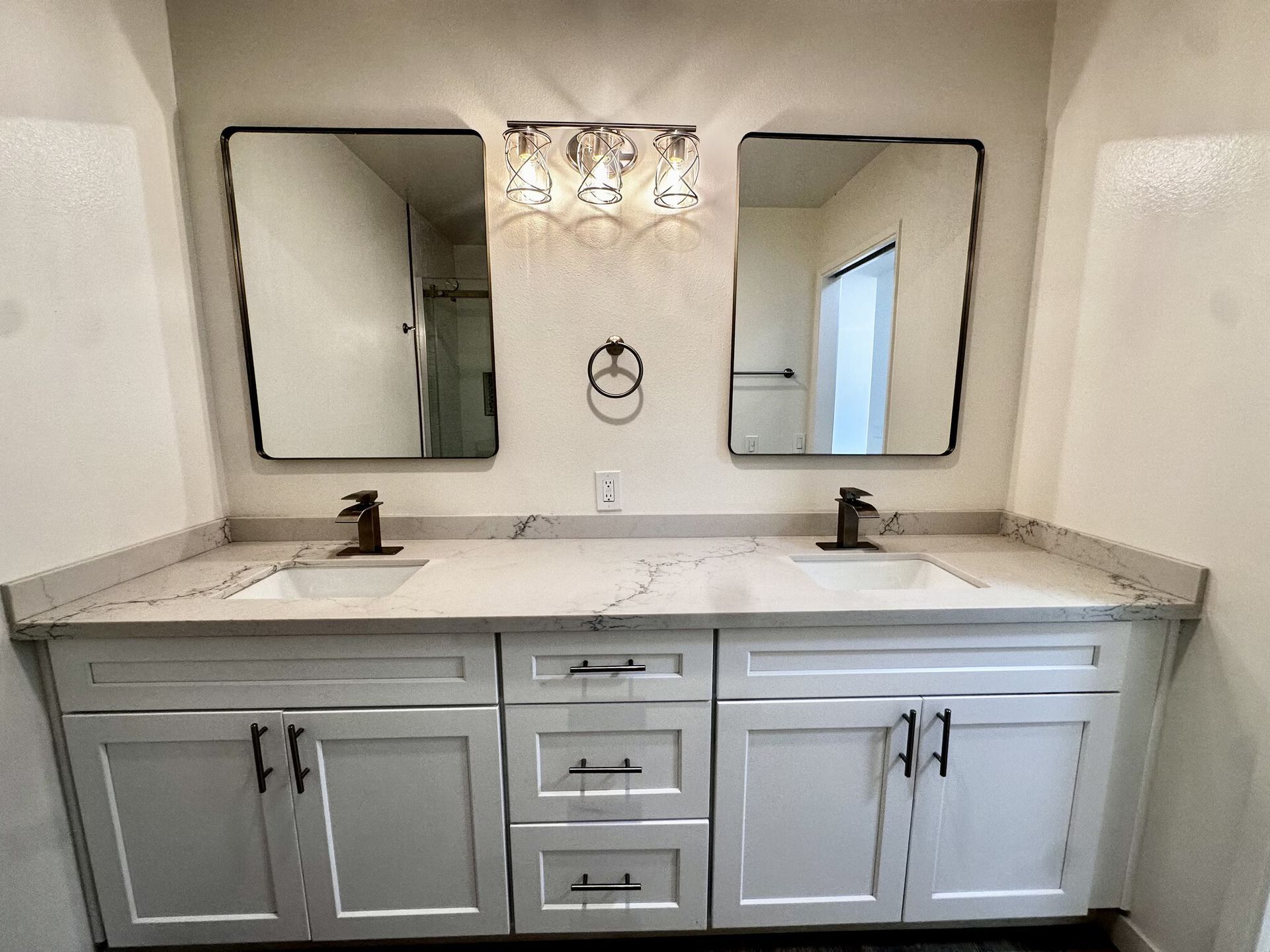 Double vanity bathroom with gray cabinets, two mirrors, and wall sconces under a bright light fixture