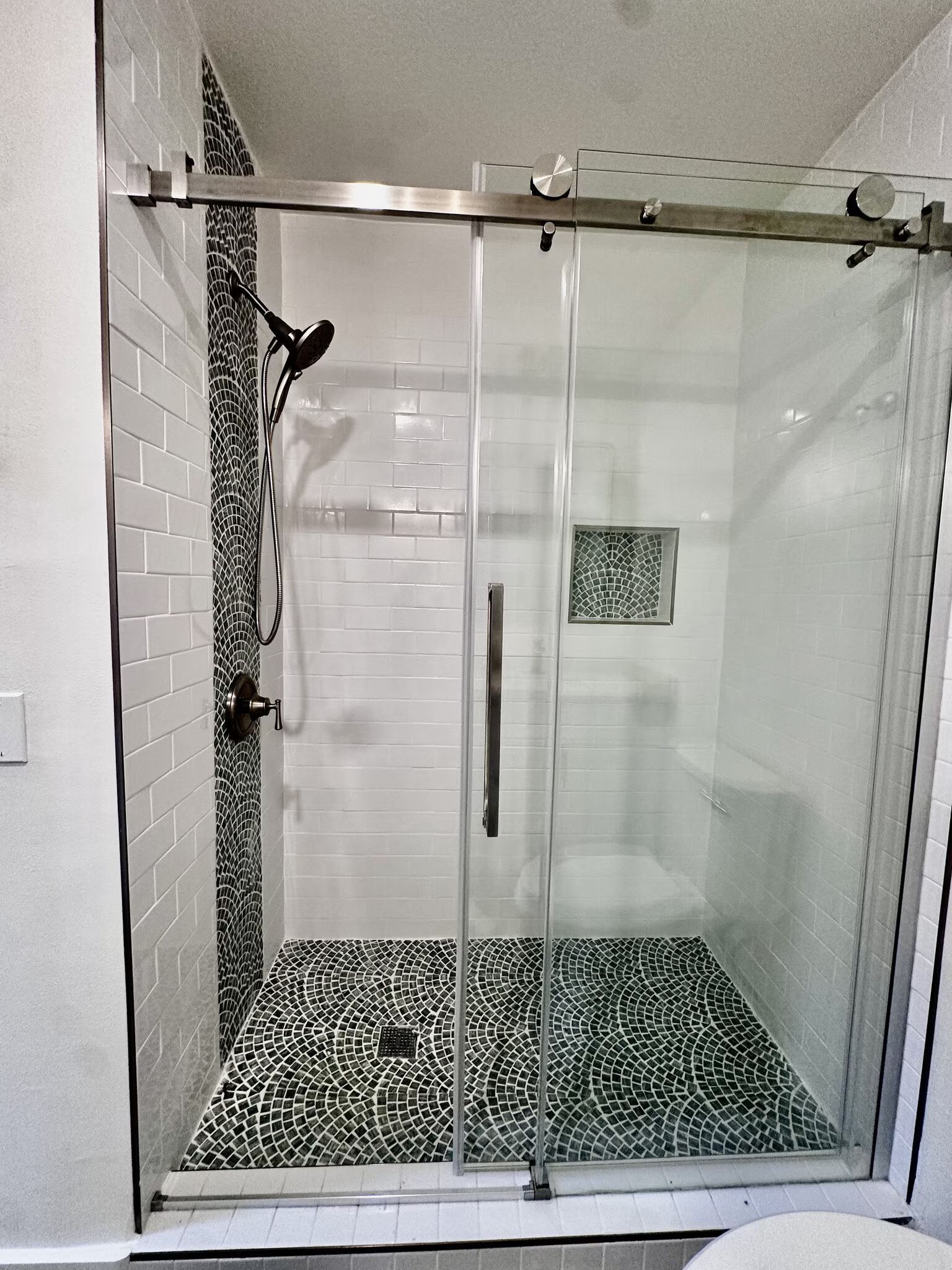 Glass walk-in shower with black-and-white pebble floor and square tile accent wall