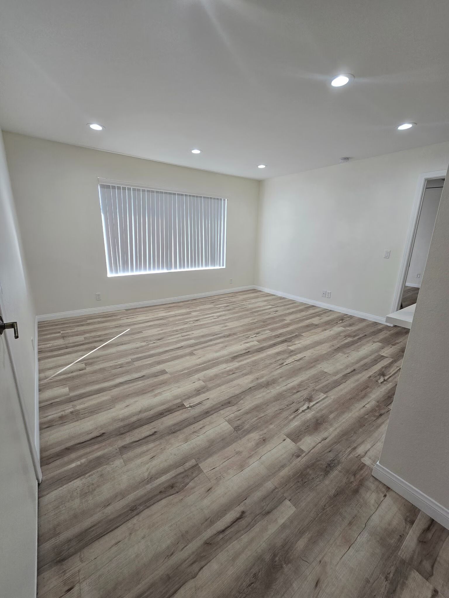 Empty room with wood-look flooring, white walls, recessed lights, and a window with blinds