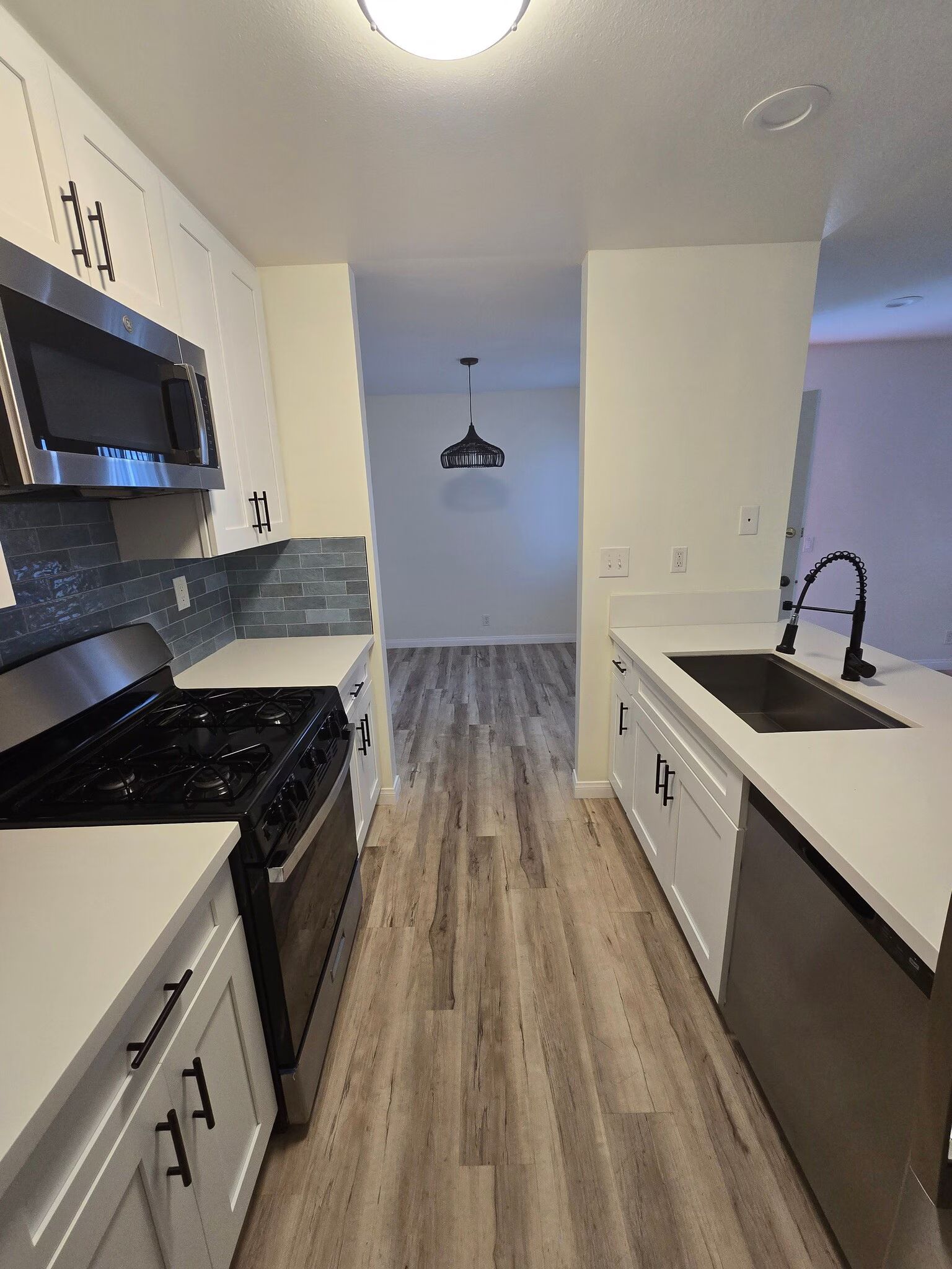 Modern galley kitchen with black appliances, white cabinets, and light wood flooring.