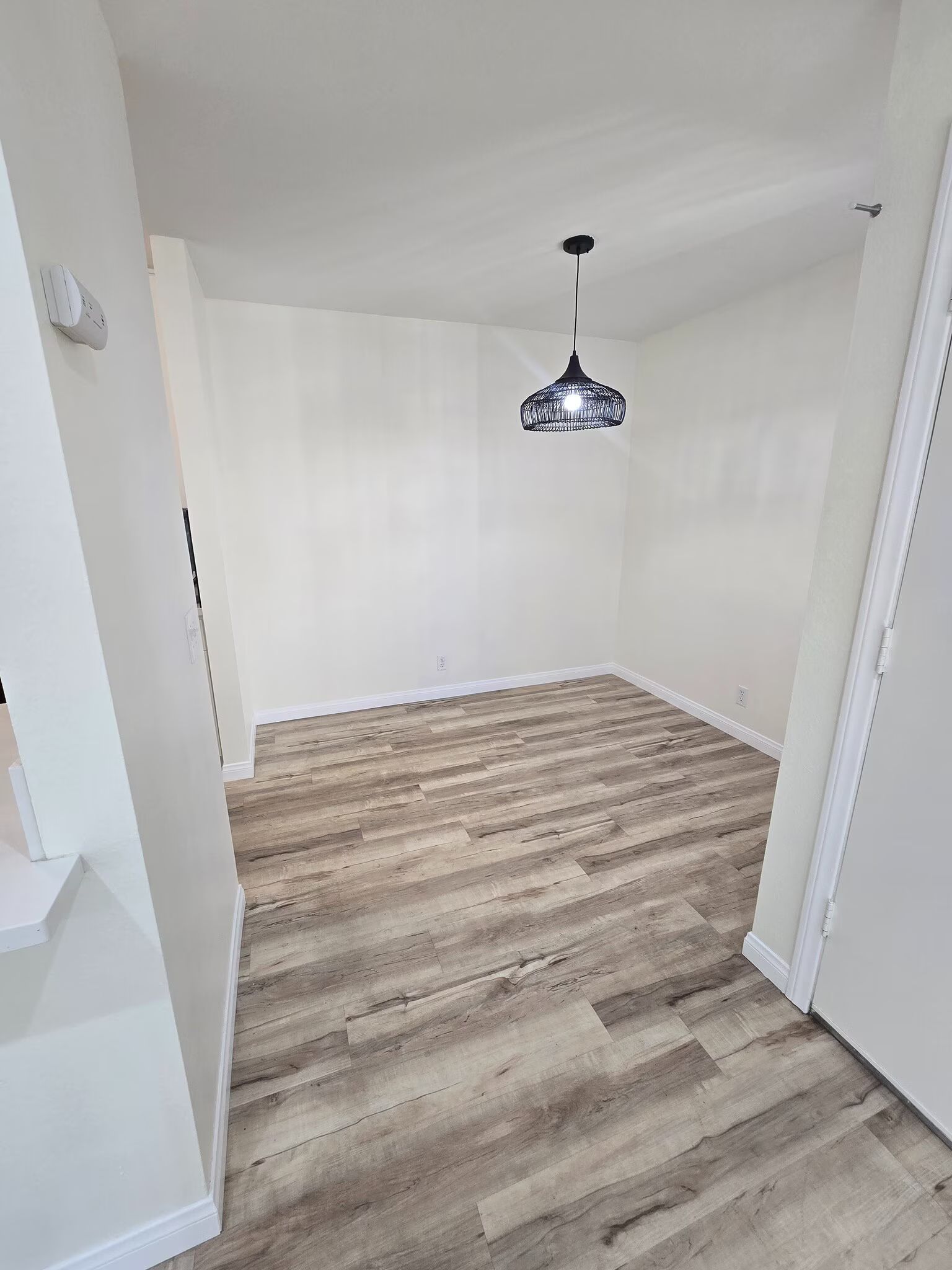 Empty dining area with wood-look floors, white walls, and a small hanging light fixture.