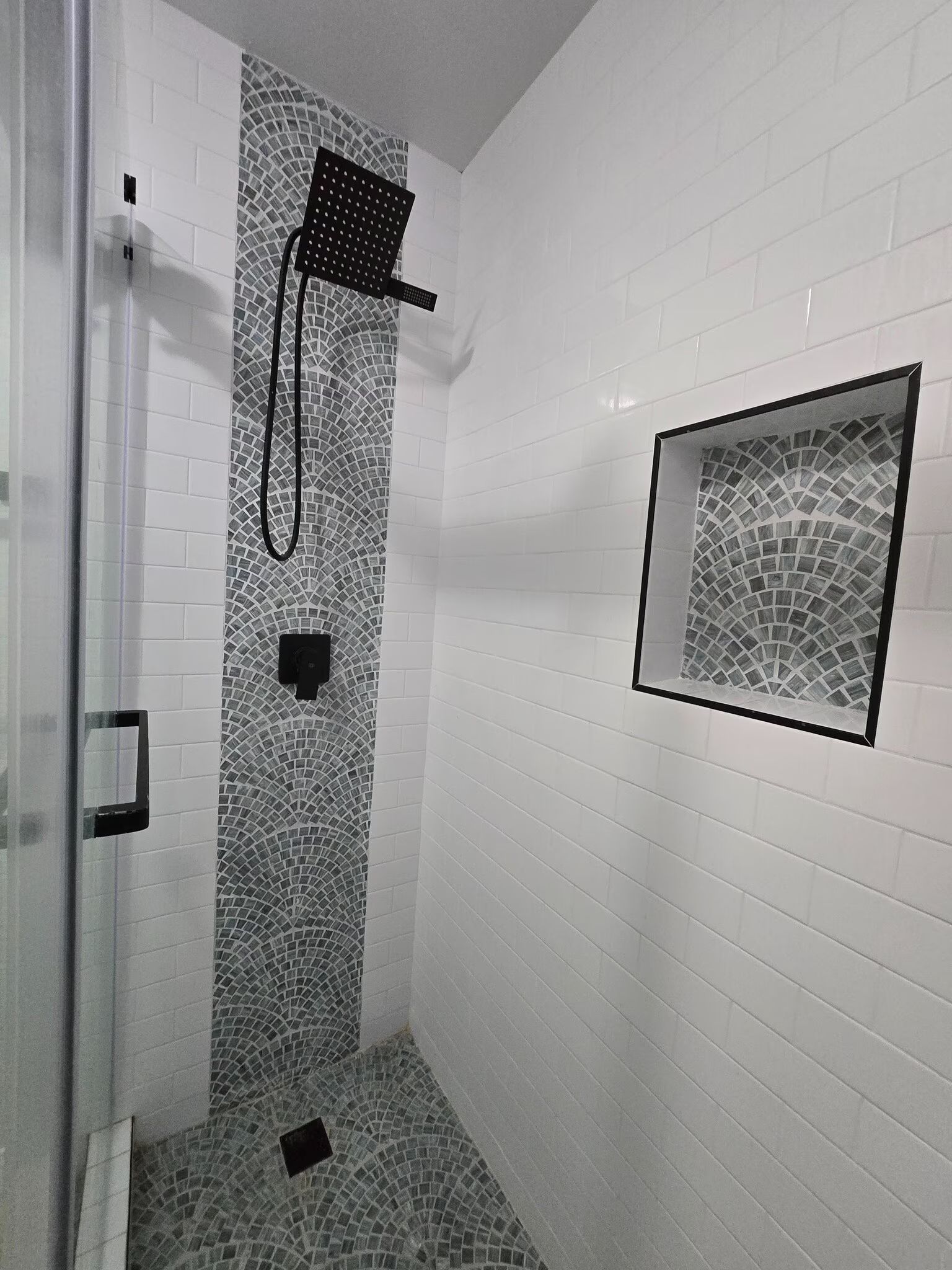 White tiled shower with glass door, black showerhead, and small frosted window.